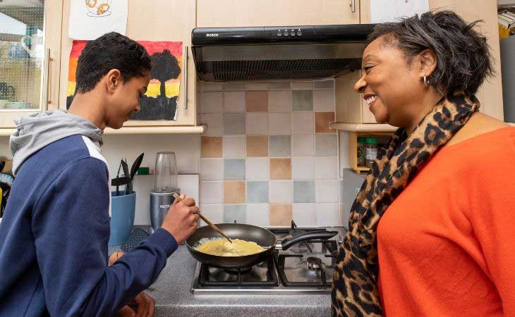 Foster carer supervising young male cooking on stove