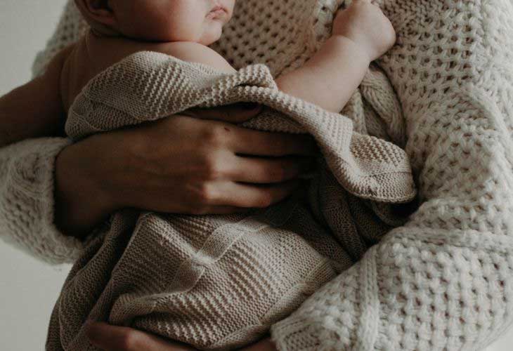 A baby wrapped in blanket in adults arms