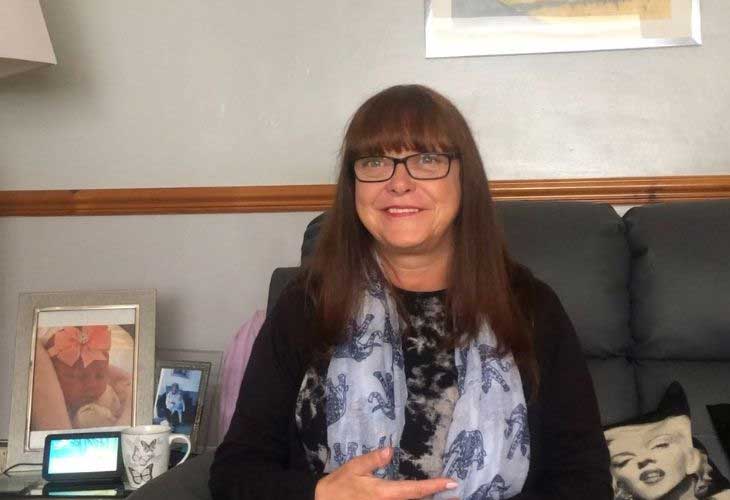 A foster carer, June, sitting on sofa and smiling